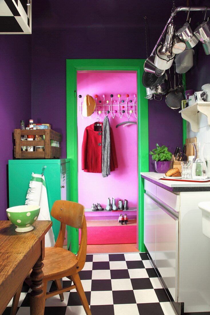 Violette Wände, grüner Metallschrank und Türrahmen in kleiner Küche mit Schachbrettmusterboden, Blick in pinkfarbene Diele