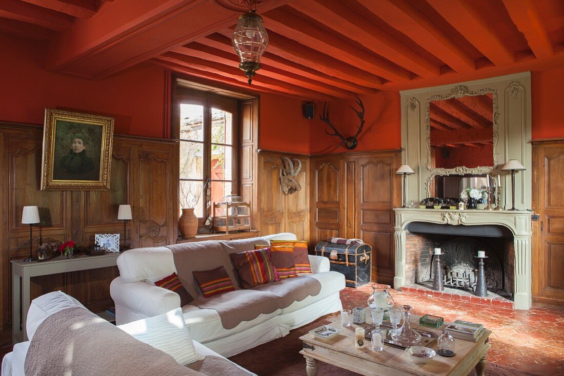 Seating area in front of fireplace in grand country house with half-height wood panelling and red-painted walls and ceiling