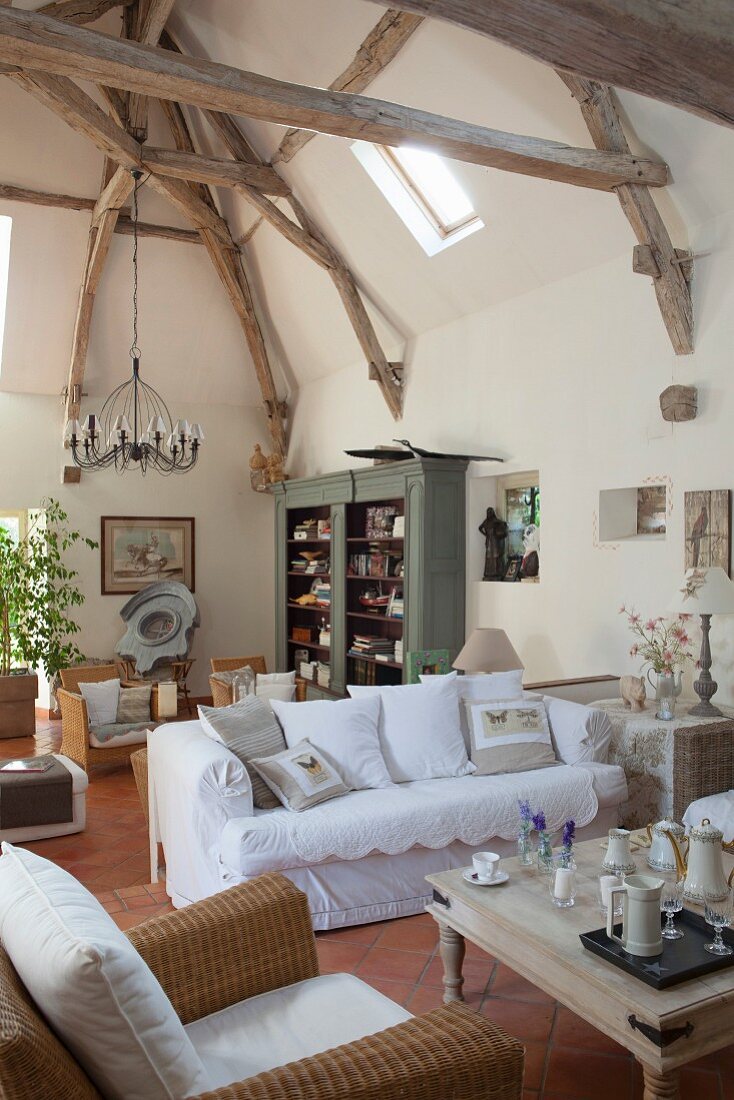 Offener Wohnraum mit sichtbarer Holz-Tragwerkskonstruktion, Loungebereich mit Rattansessel und weißem Hussensofa