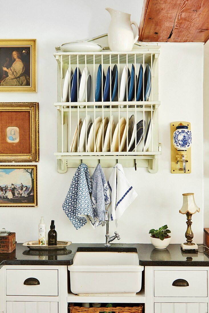 Vintage plate rack and gilt-framed pictures above retro sink in black worksurface