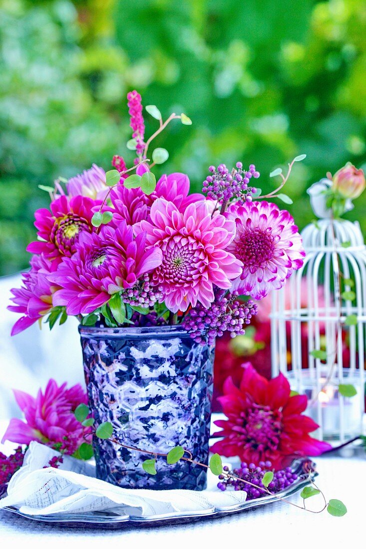 Bouquet of pink dahlias in silvered glass vase on table outdoors