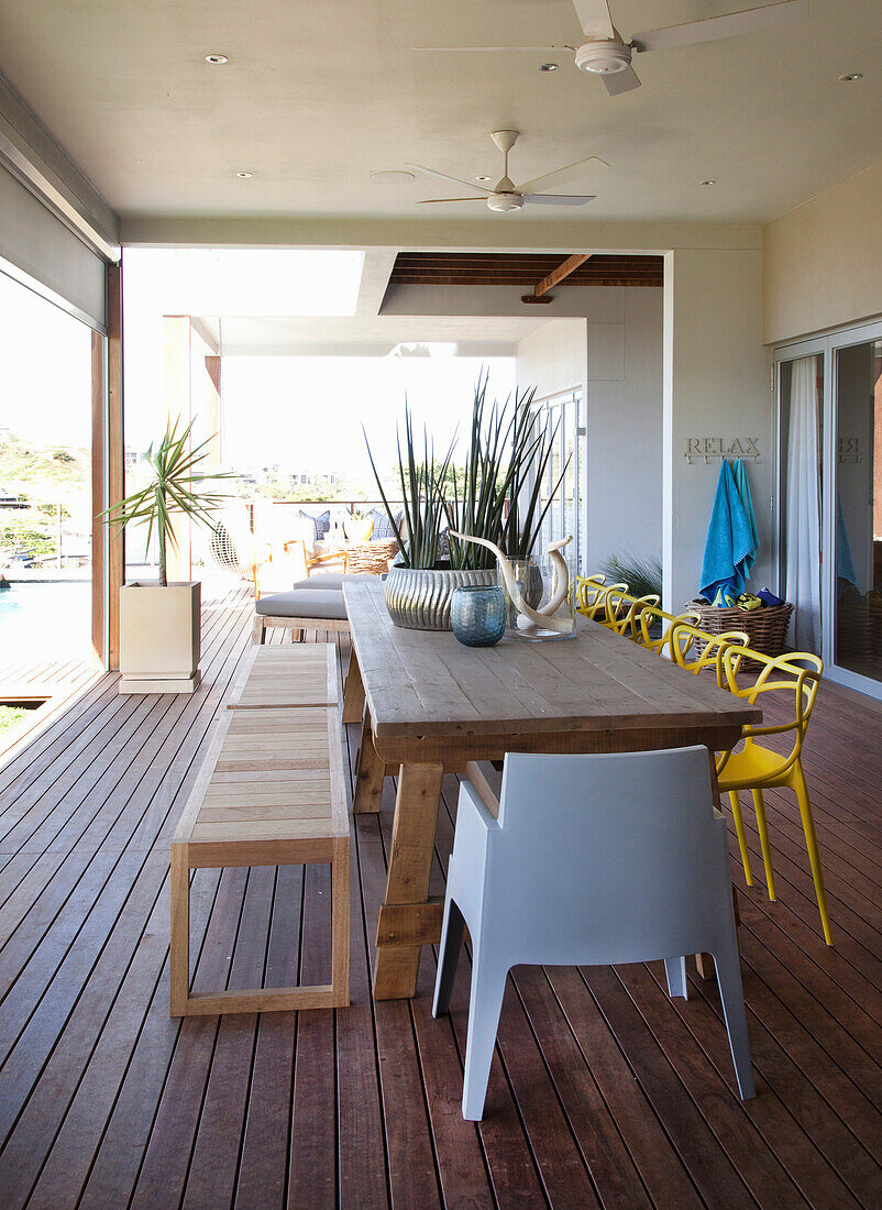 Terrasse mit Esstisch, Holzbank und gelben Stühlen, Deckenventilator und Pflanzendekoration