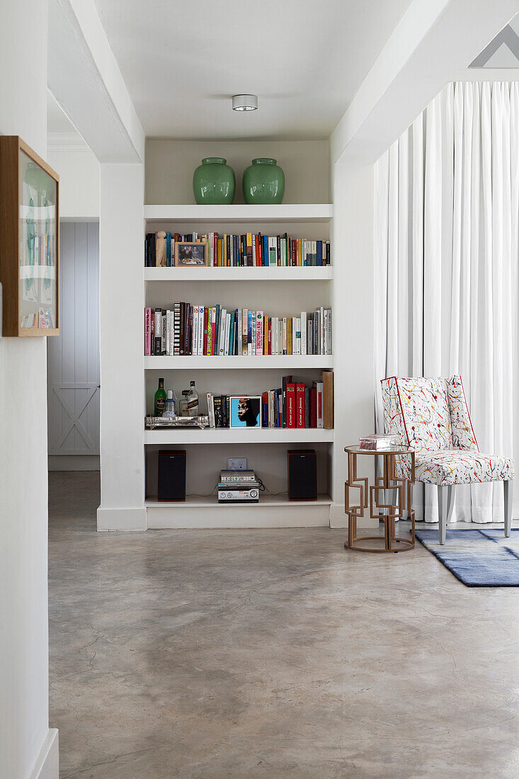 Weiße Einbauregalwand mit Büchern und grünen Vasen, Sessel mit Blumenmuster