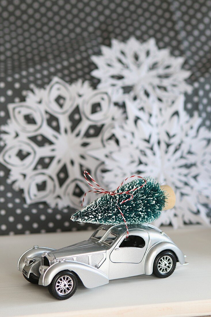 Spielzeugauto mit Weihnachtsbäumchen auf Autodach, vor Papiersternen