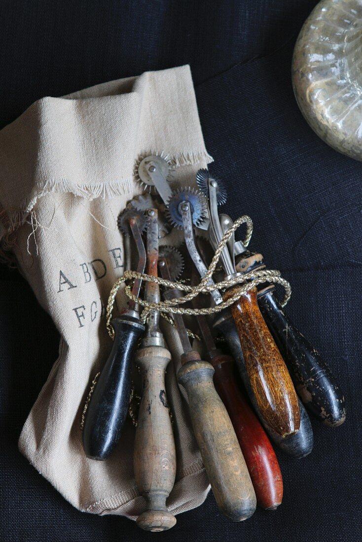Mit Goldschnur umwickelte, antike Teigrädchen auf handgestempeltem Sack
