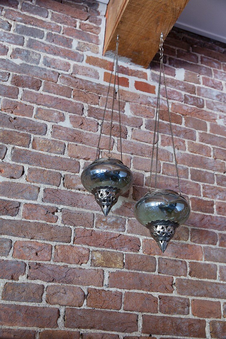 Oriental lanterns hanging from wooden beam against brick wall