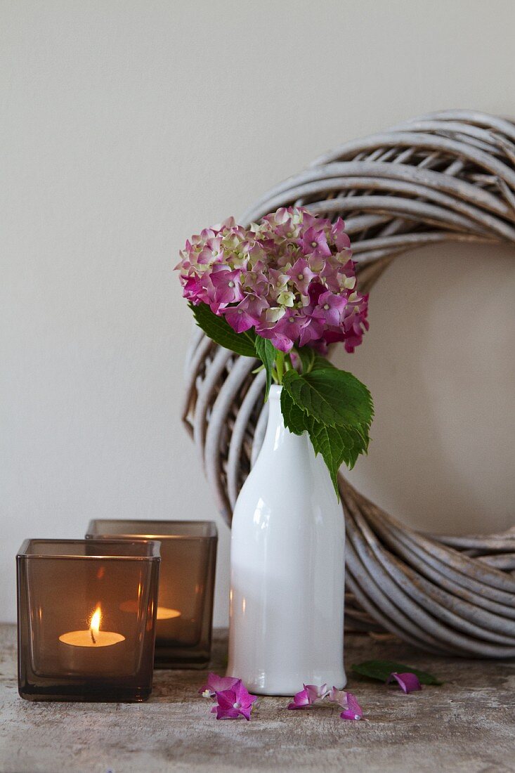Smoked glass tealight holders and hydrangea in white, retro vase in front of wreath of pale willow