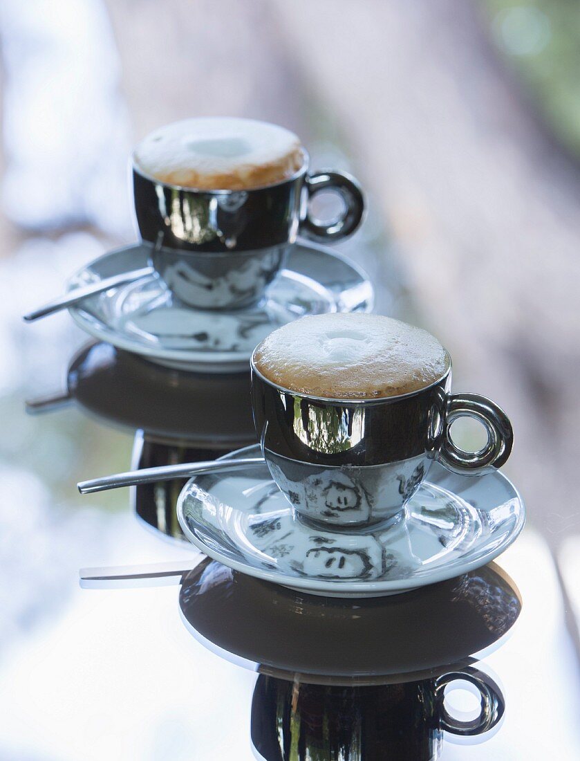 Cappuccino in designer cups on table with mirrored top