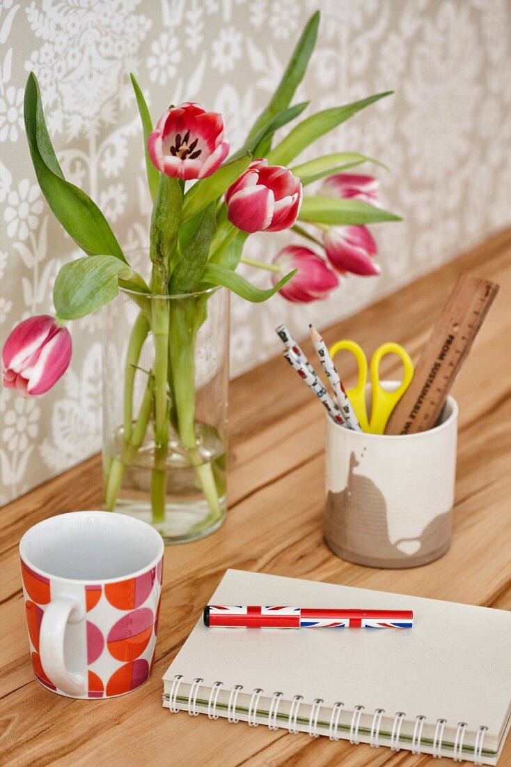 Tulips and mug on desk with pronounced wood grain against wall with pale, patterned wallpaper