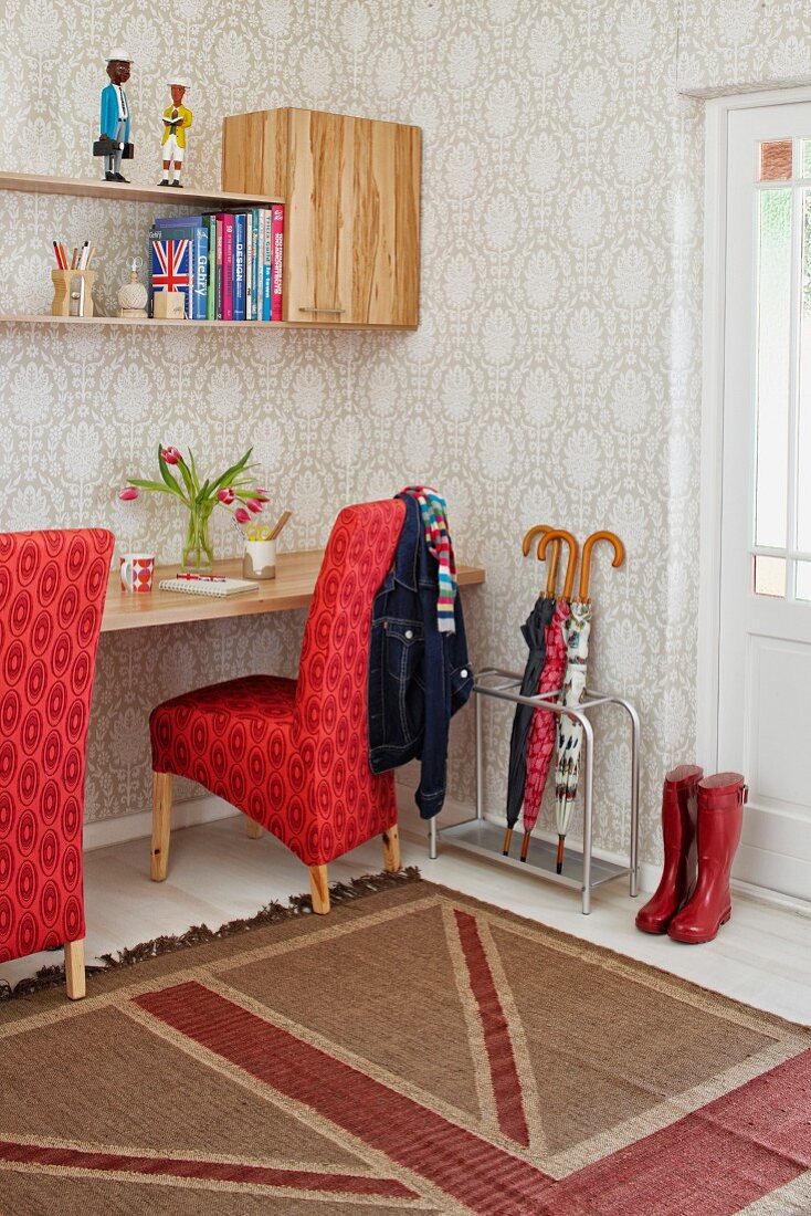 Schreibtisch mit rot gepolsterten Stühlen und Wandboard vor heller Tapete