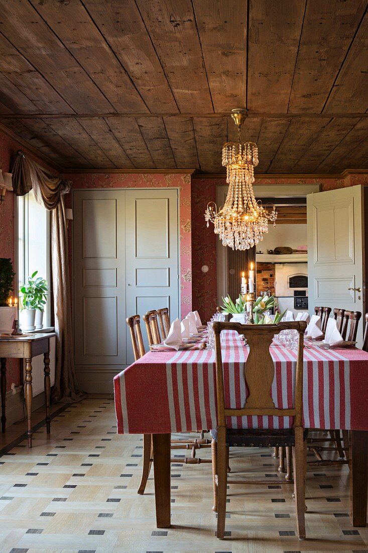 Chandelier, old wooden chairs and striped cloth on table in cosy dining room