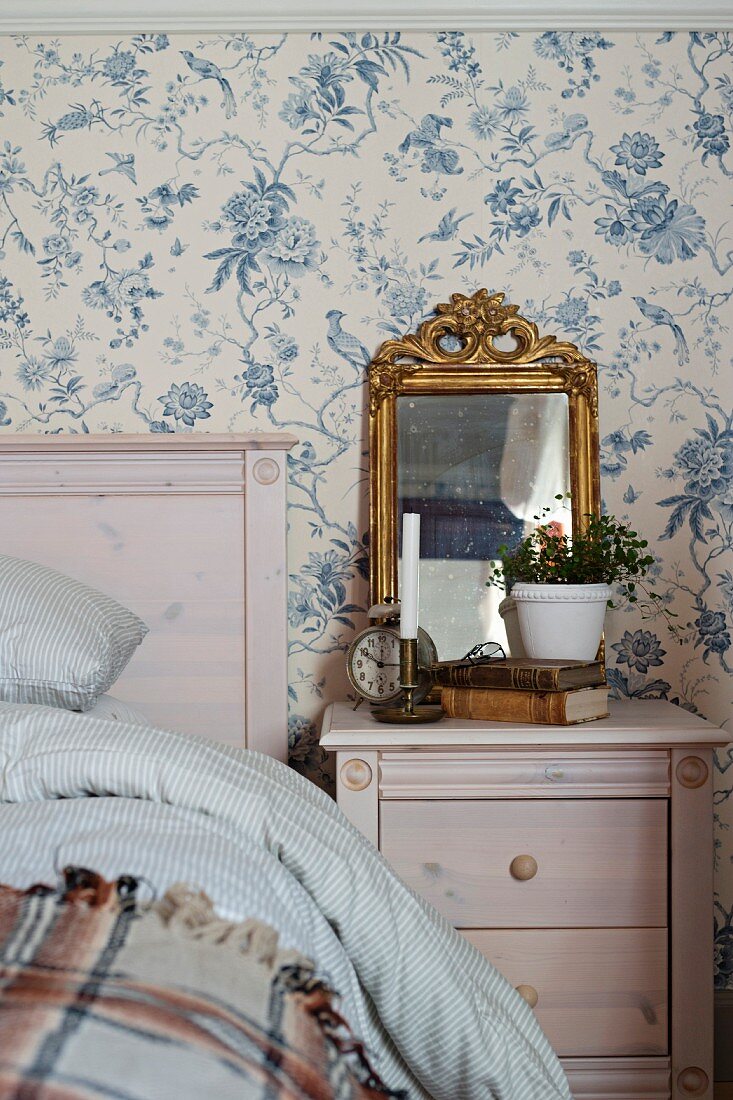 Nachtkästchen mit Vintage Deko neben Bett, Tapetenwand mit nostalgischem, floralem Muster