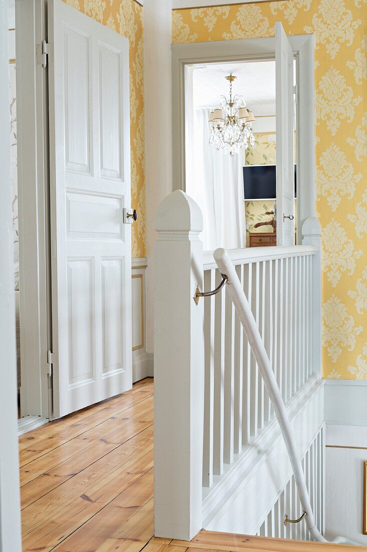 Ländliches Treppenhaus mit weiss lackierter Holztreppe und gelber Ornamentmustertapete