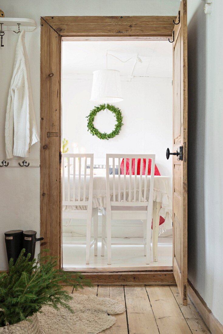 Korb mit Tannenzweigen auf Holzdielenboden im Vorraum, Blick durch offene Tür auf Essplatz und Wandkranz