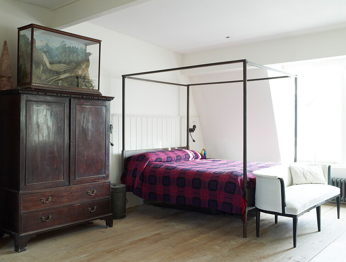 Simple four-poster bed next to old wooden cabinet