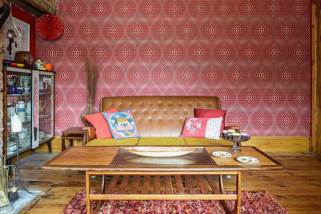 Old coffee table and leather sofa in front of red patterned wallpaper