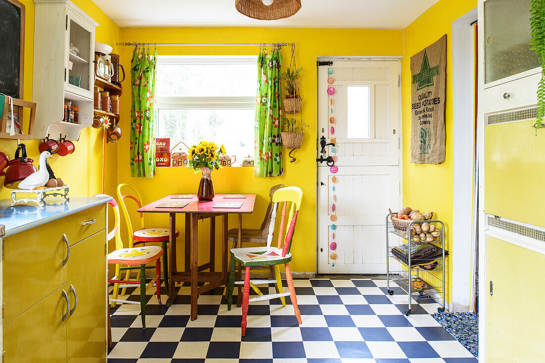 Colourful chairs in yellow kitchen-dining room with chequered floor