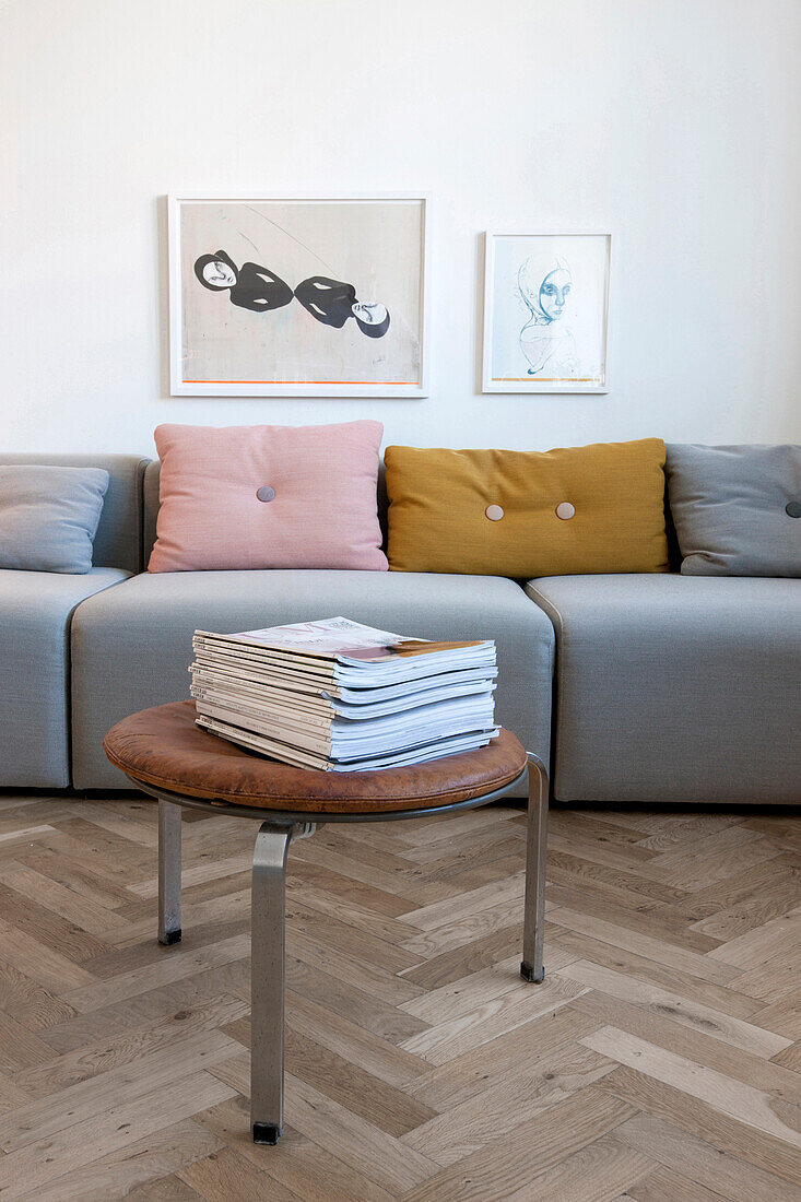 Hocker mit Lederpolster und Zeitschriftenstapel vor dem modernen Sofa