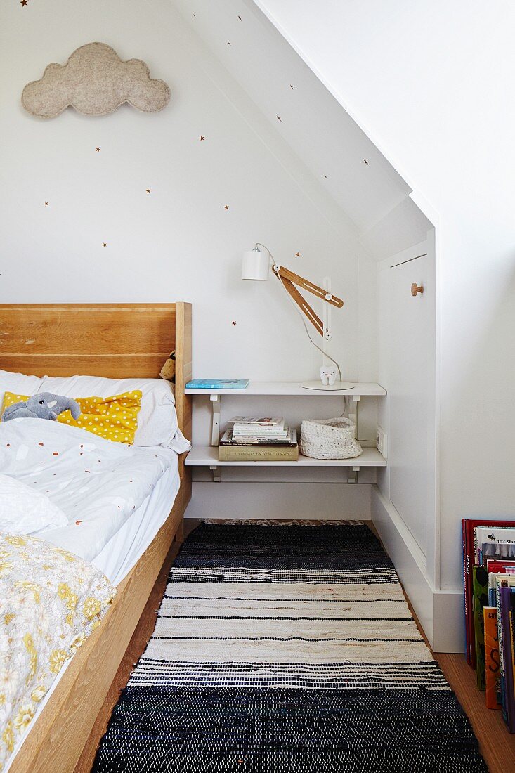 Wood.framed bed, bedside shelves and blac and white rug in child's attic bedroom