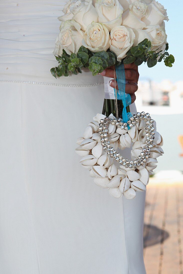 Bride holding bouquet of white roses with heart made from seashells and jingle bells