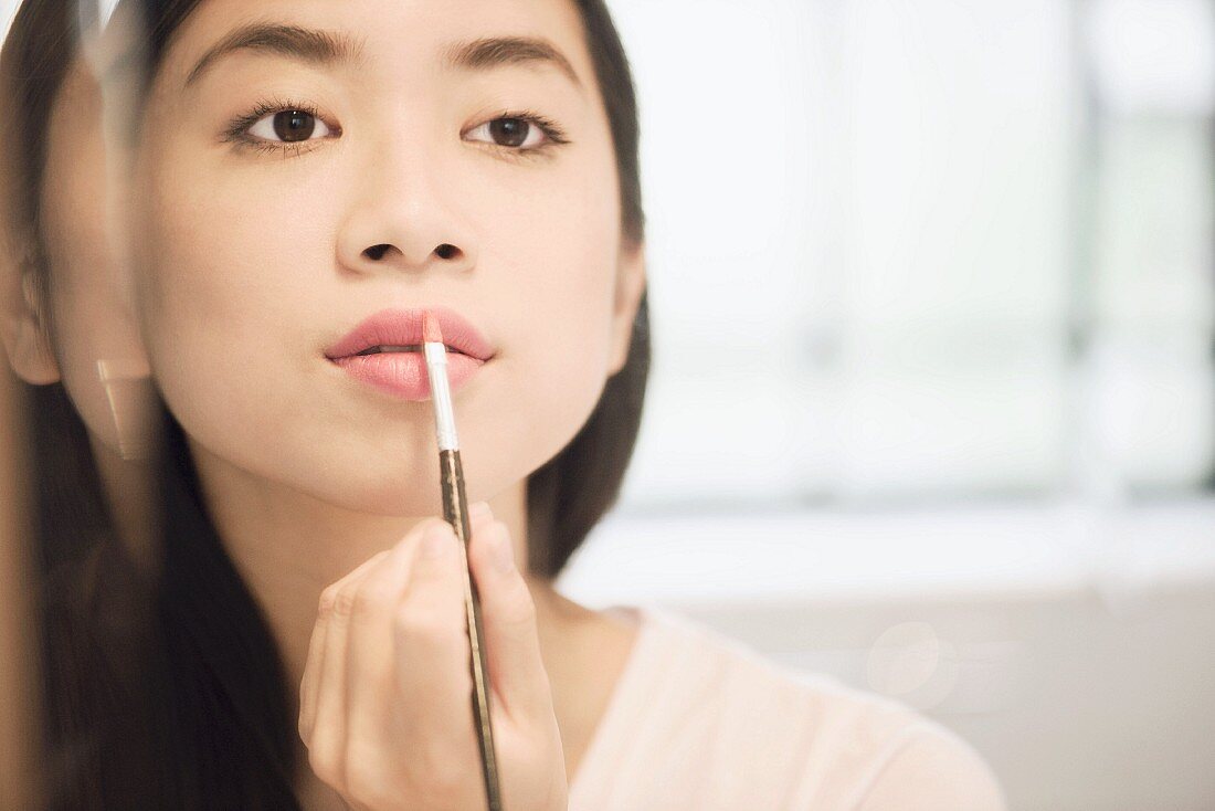 Asiatische Frau schminkt sich die Lippen mit Pinsel