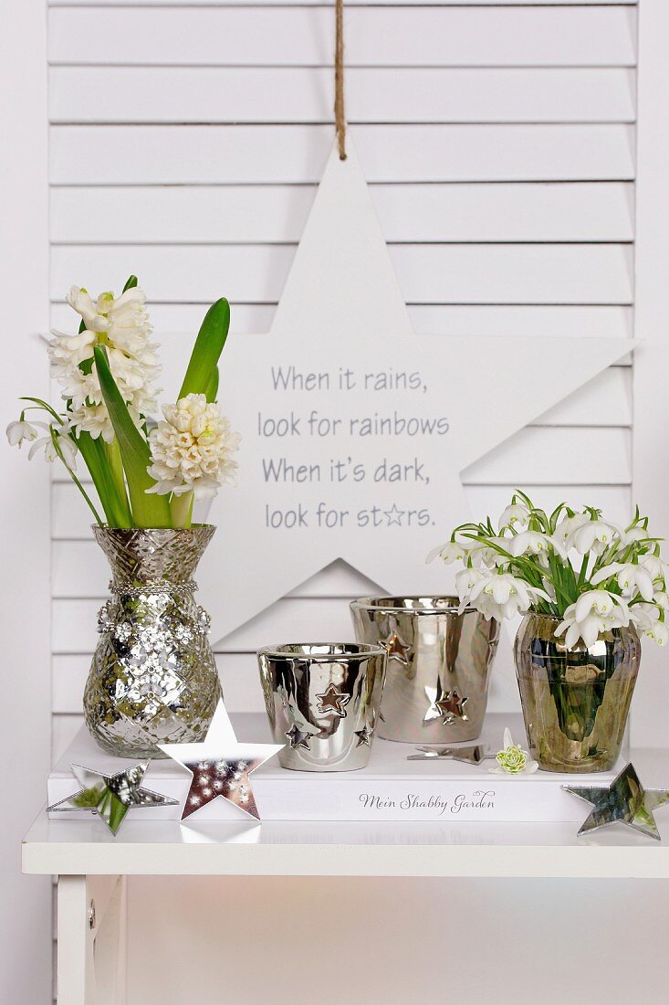 White hyacinths, snowdrops and silver-coloured containers below motto written on star-shaped decoration