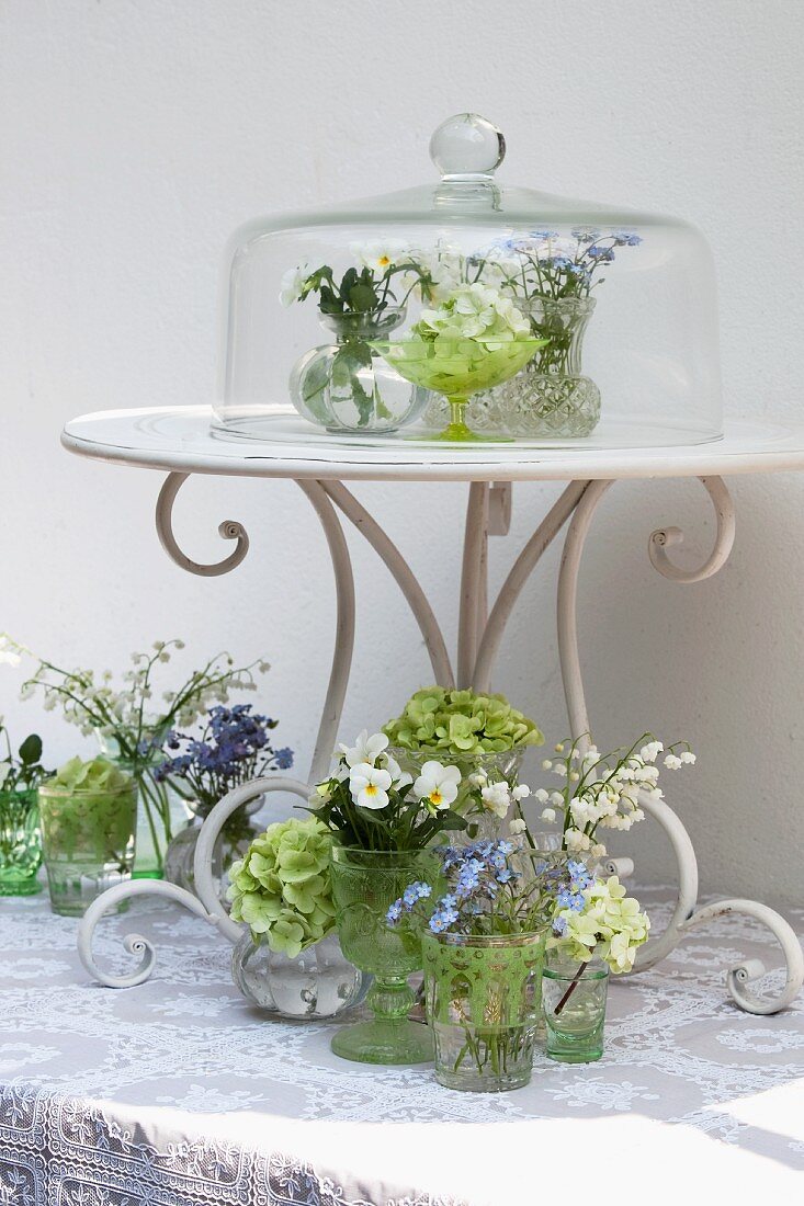 Arrangement von Miniväschen mit Frühlingsblumen auf Tisch & unter Glasglocke