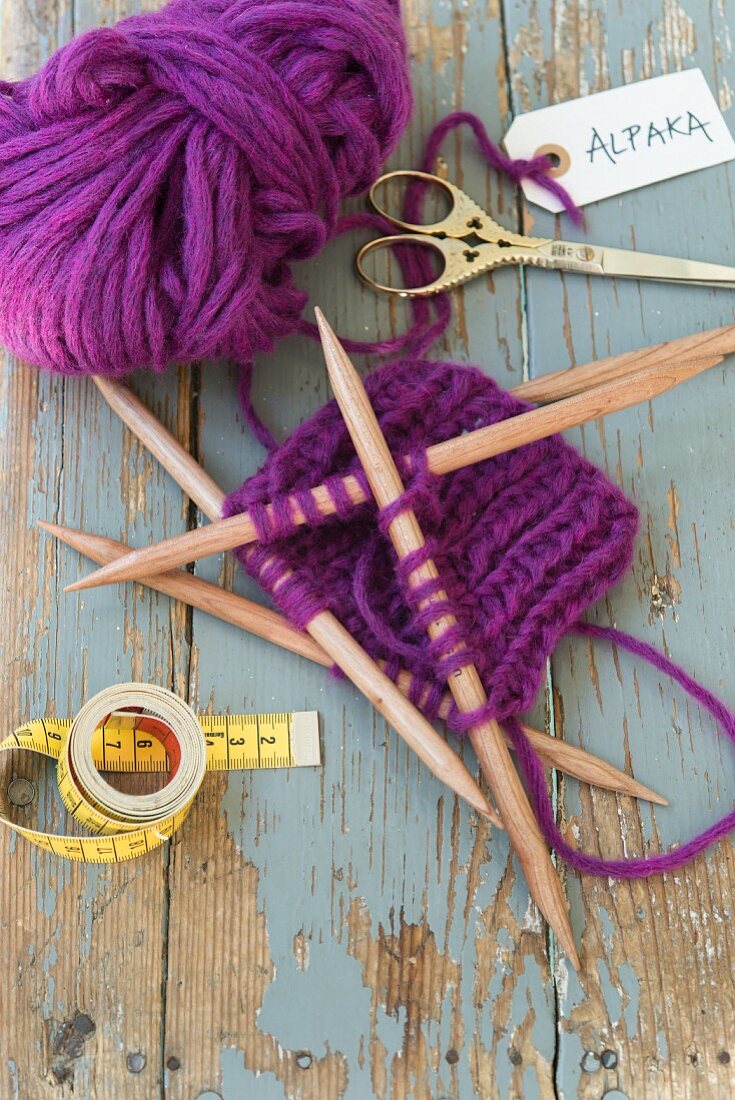 A piece of purple alpaca wool knitting with wooden needles