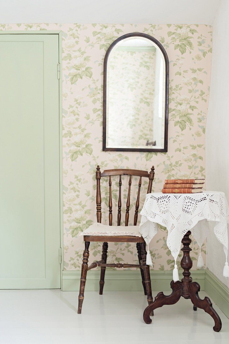 Stuhl mit gedrechselten Beinen und Beistelltisch aus dunklem Holz mit weisser Spitzendecke in Zimmerecke, an tapezierter Wand Wandspiegel