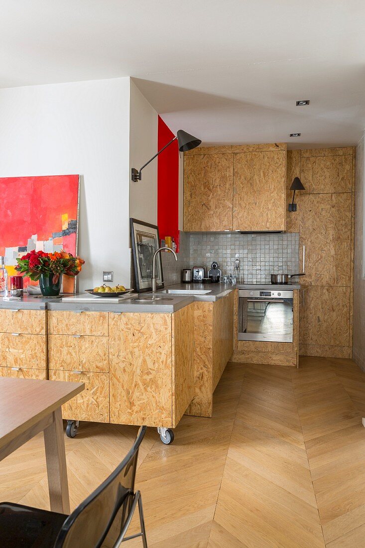 Moderne Küche mit Fischgrätparkett, im Hintergrund Küchenzeile mit mobilem Schrankmodul, Schrankfront aus OSB-Platten