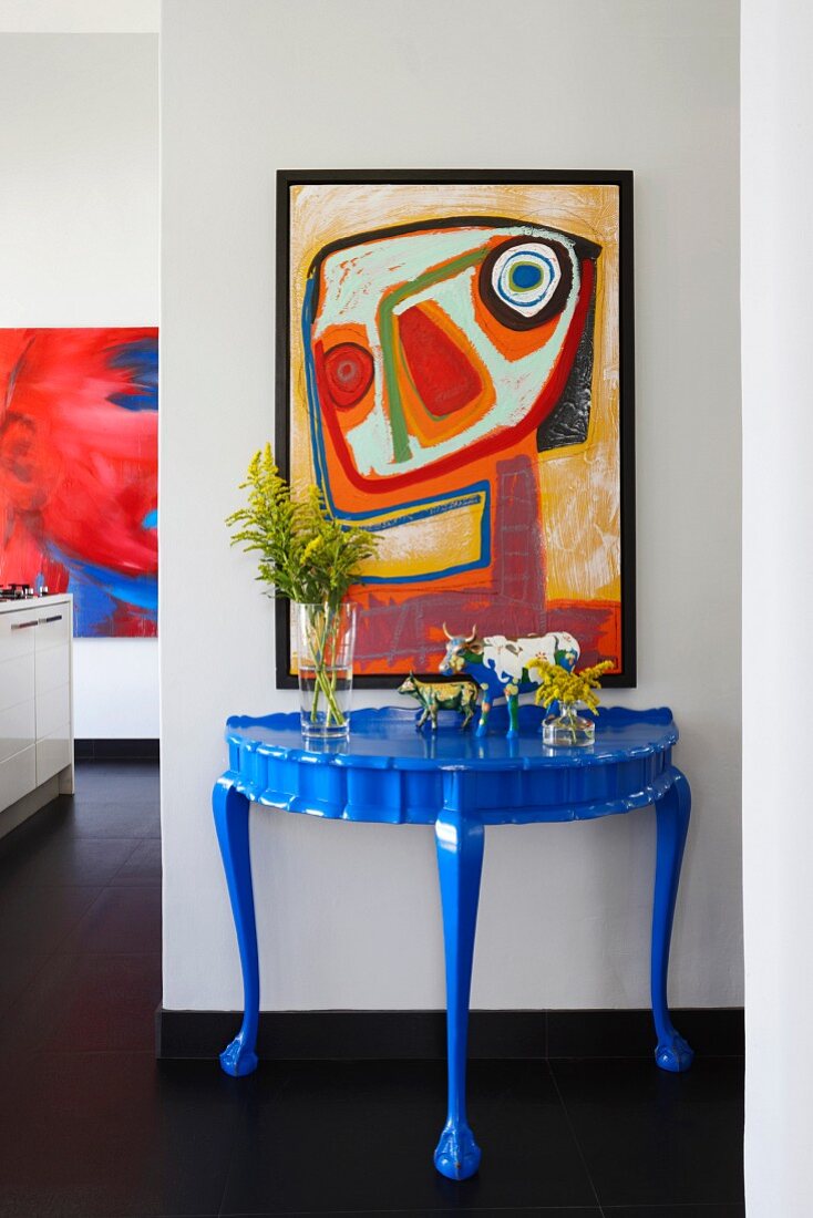 Blue-painted postmodern console table below modern artwork on wall