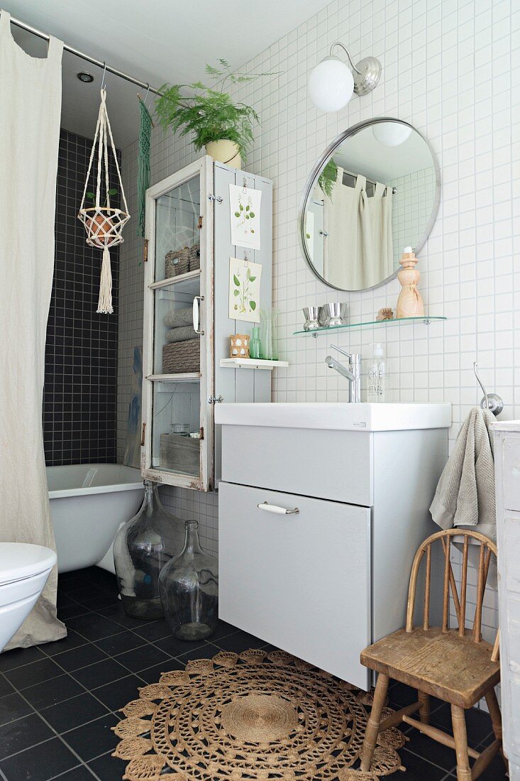 Schlichtes Waschtischmöbel unter rundem Spiegel an weiss gefliester Wand im Bad, Badewanne hinter Vorhang