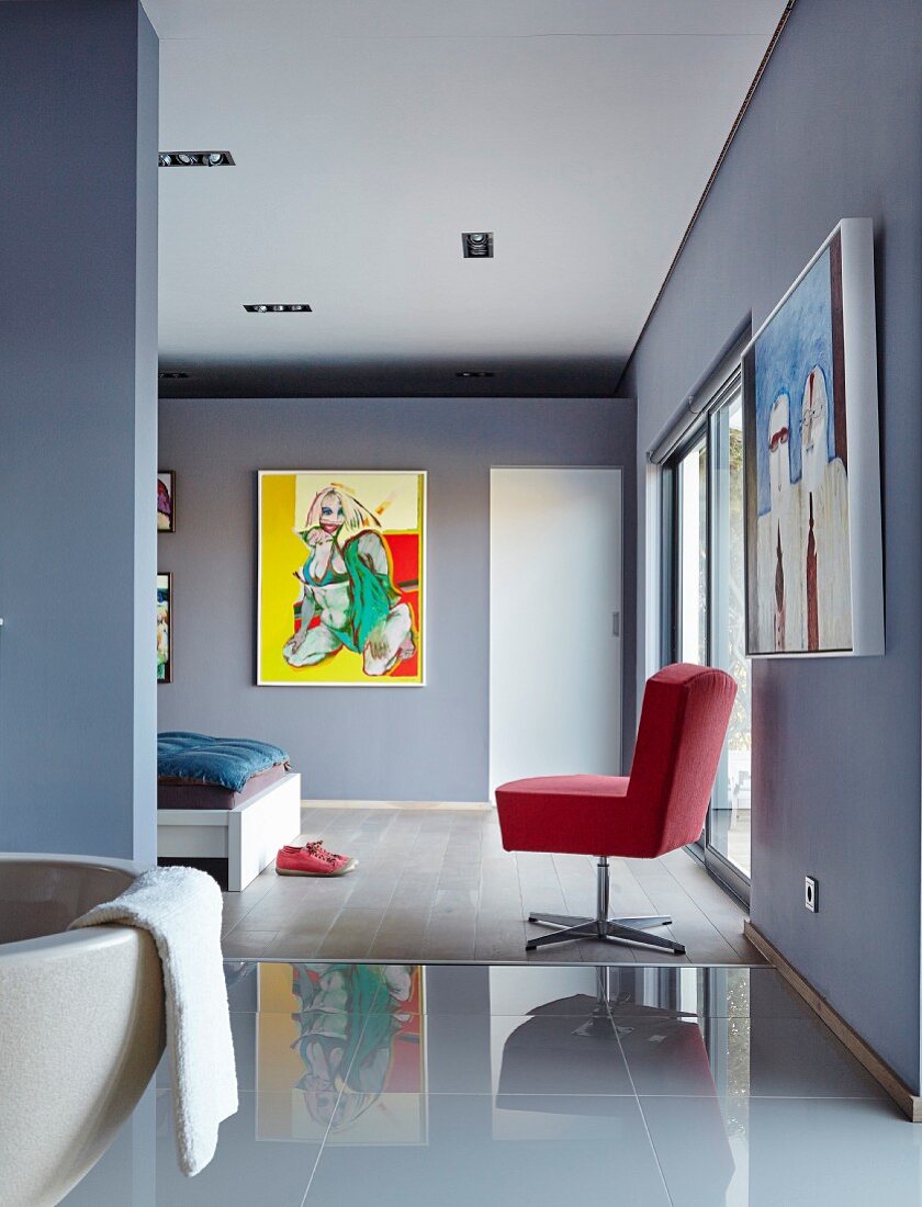 Ensuite bathroom with glossy tiled floor leading into blue-grey bedroom with red swivel chair and modern painting