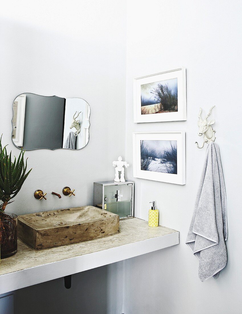 Washstand with concrete sink below vintage mirror and framed photos on walls