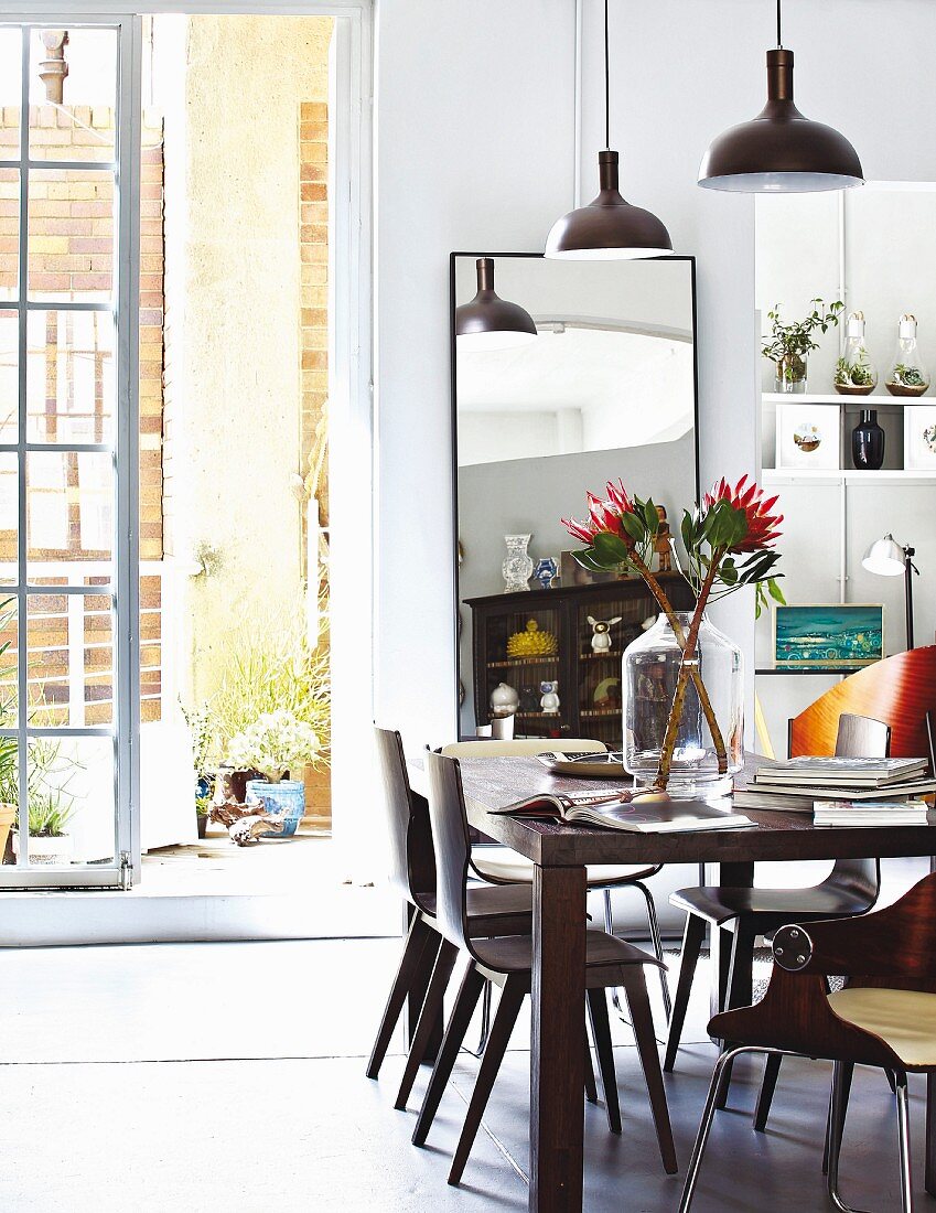 Dining table decorated with proteas below industrial-style pendant lamps in front of open French windows