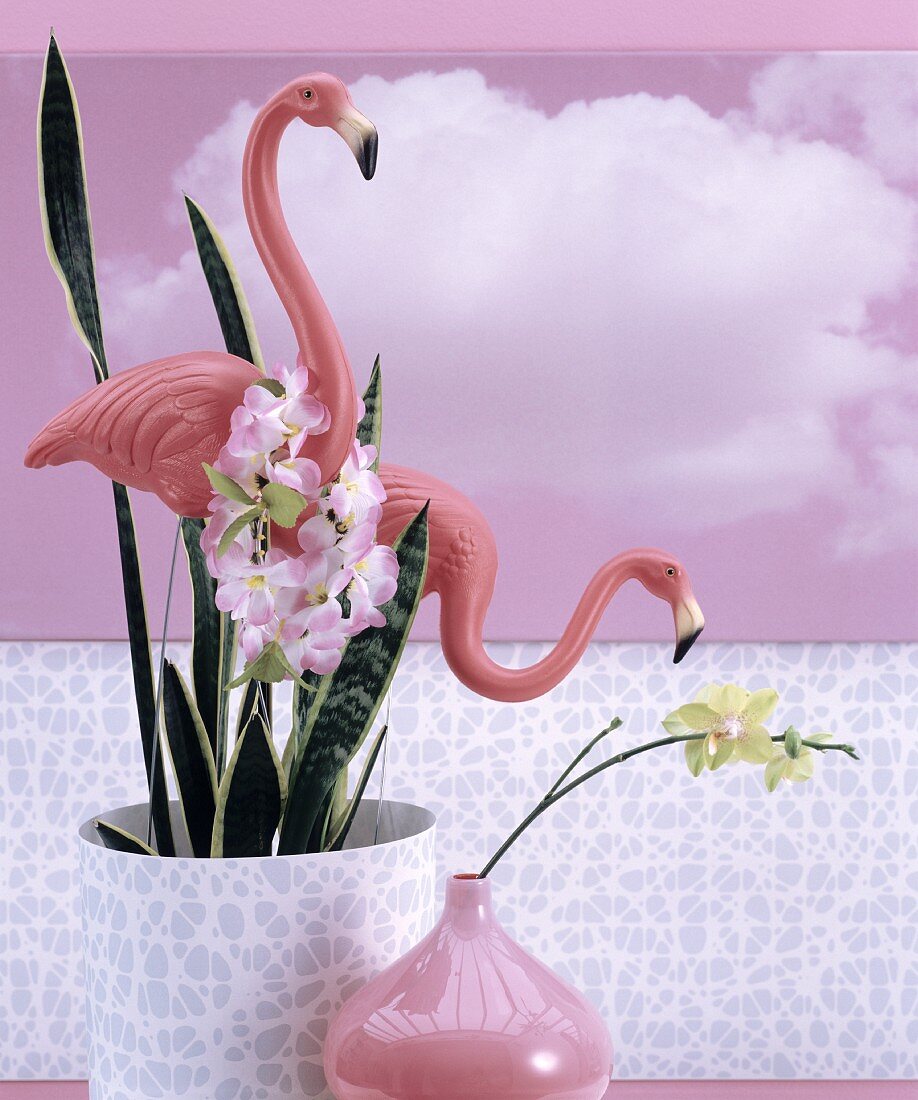 Zimmerpflanze mit Kunststoff-Flamingos, pinkfarbene Vase und rosa Fototapete mit Wolkenmotiv