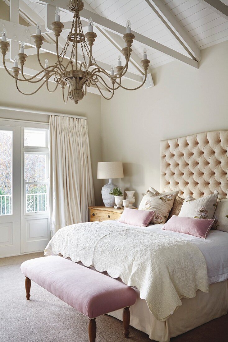 Chandelier above double bed with button-tufted headboard and antique bedroom bench
