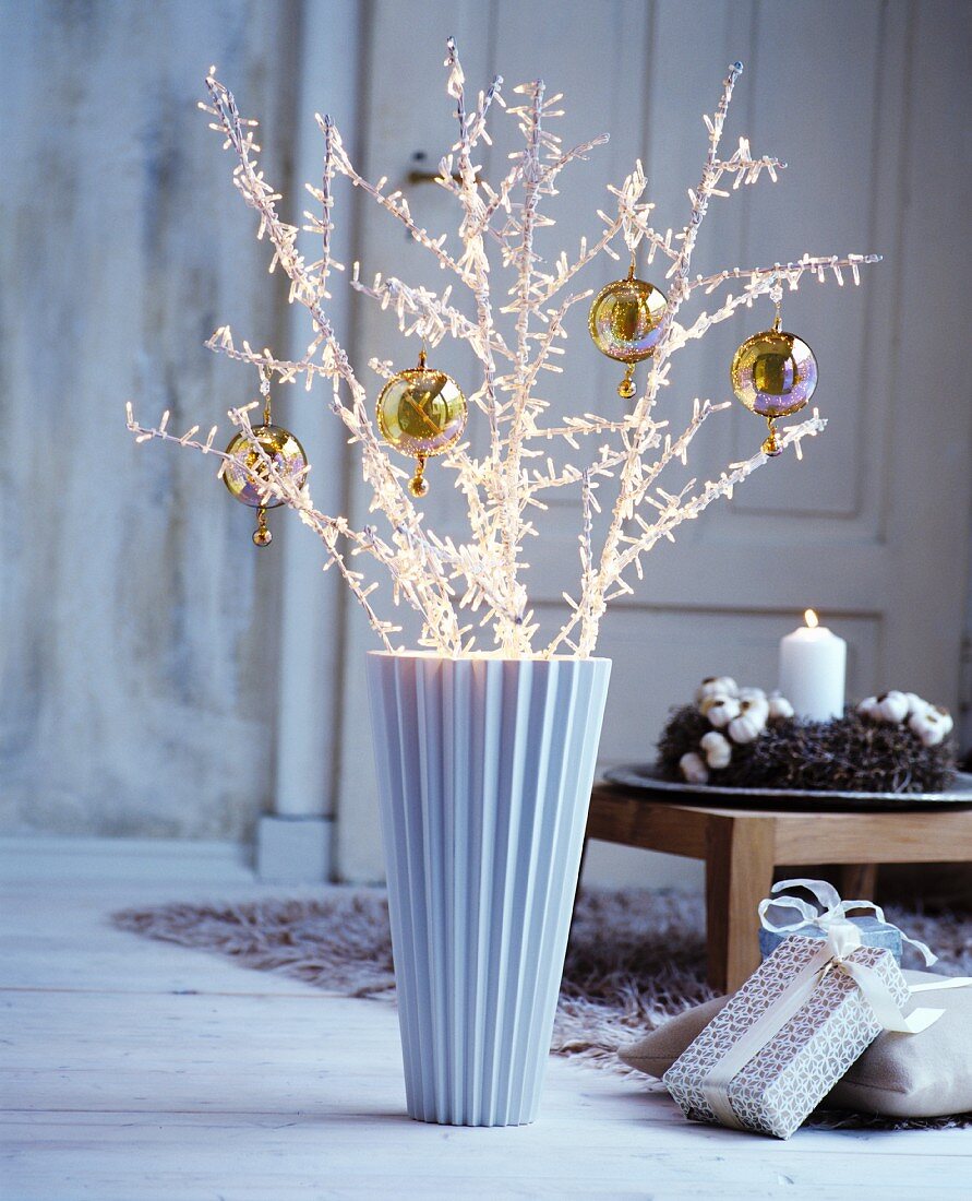 Twigs covered in fairy lights and decorated with baubles in floor vase