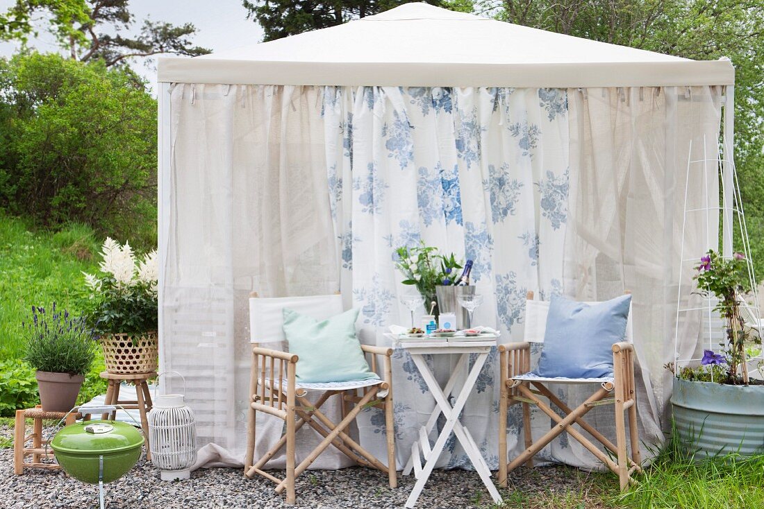 Tisch für Zwei vor romantischem Gartenpavillon mit luftigem Stoff