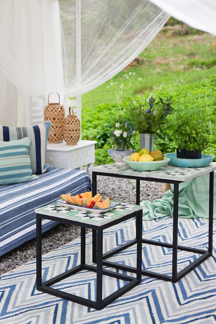Zweiteiliges Beistelltisch-Set mit Musterfliesen als Tischplatte auf Teppich in möbliertem Gartenpavillon