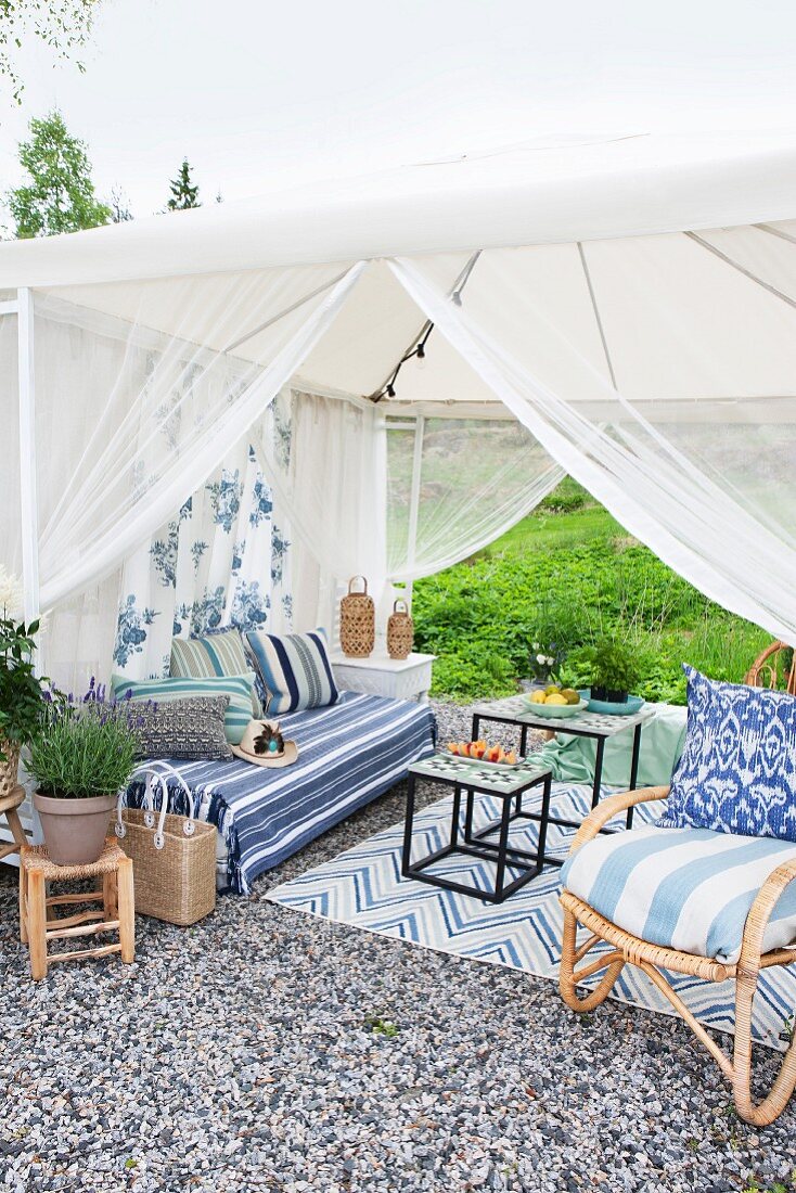 Lounge in möbliertem Gartenpavillon mit luftigem Stoffbezug auf gekiestem Platz