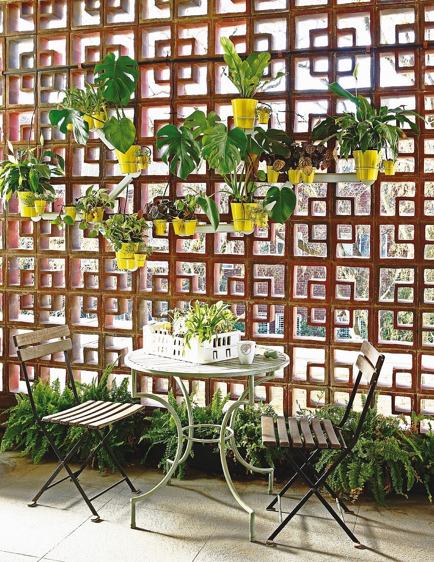 Tisch mit zwei Stühlen auf der Terrasse vor dekorativer Sichtschutzwand mit Lochmuster, daran aufgehängte Blumentöpfe
