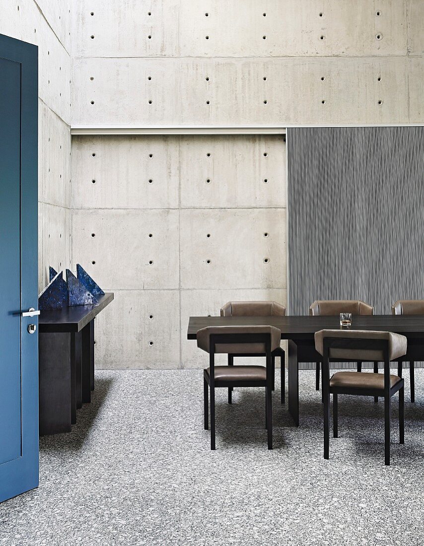 Dining room with concrete walls, dark furniture and blue door