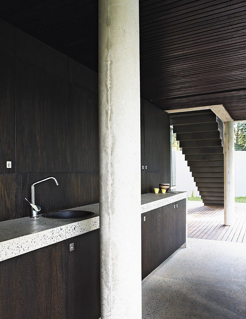 Minimalistische Küche mit Fronten aus dunklem Holz, Betonsäulen und Fensterfront