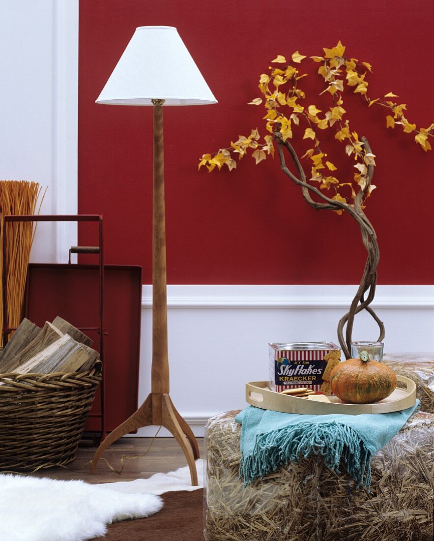 Autumnal home accessories: standard lamp with wooden base, transparent plastic pouffe stuffed with straw and branches decorated with garlands of leaves