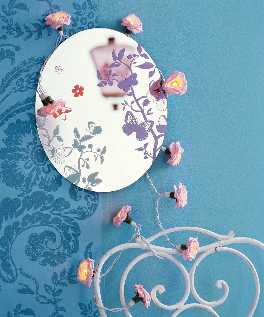 Runder Spiegel mit Schmetterlingsmotiv und Blüten-Lichterkette an blauer Wand