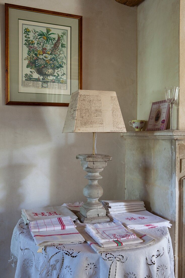 Table lamp with turned base amongst folded tea towels and tablecloths on side table in corner