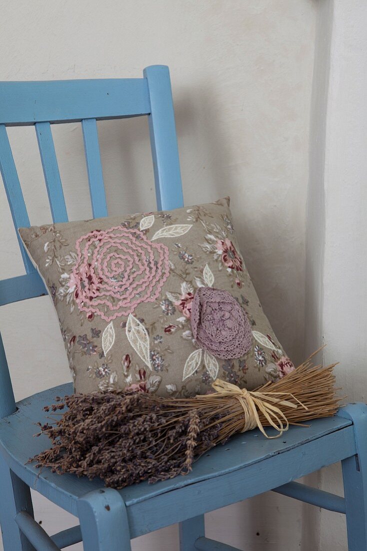Getrockneter Lavendelstrauss und Kissen mit Stickereien auf blau lackiertem Küchenstuhl