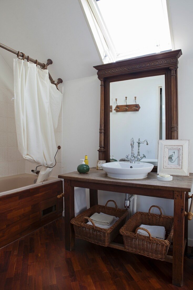 Waschtisch aus dunklem Holz vor Wandspiegel, oberhalb Dachfenster, seitlich eingebaute Badewanne mit Holzverkleidung und Duschvorhang