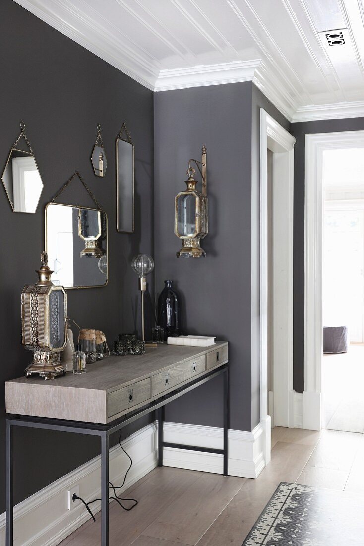 Modern console table with wooden body on metal frames below collection of vintage mirrors on anthracite wall